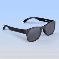 Roshambo Baby black sun glasses with grey lens agains blue backdrop
